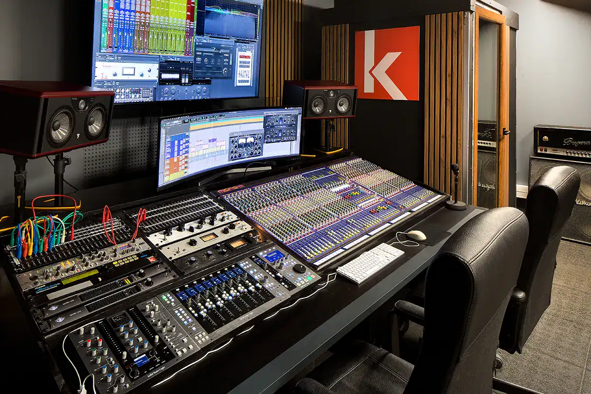 Un studio mixage dolby atmos avec une grande table de mixage, des écrans affichant des logiciels audio, et des haut-parleurs de monitoring.
